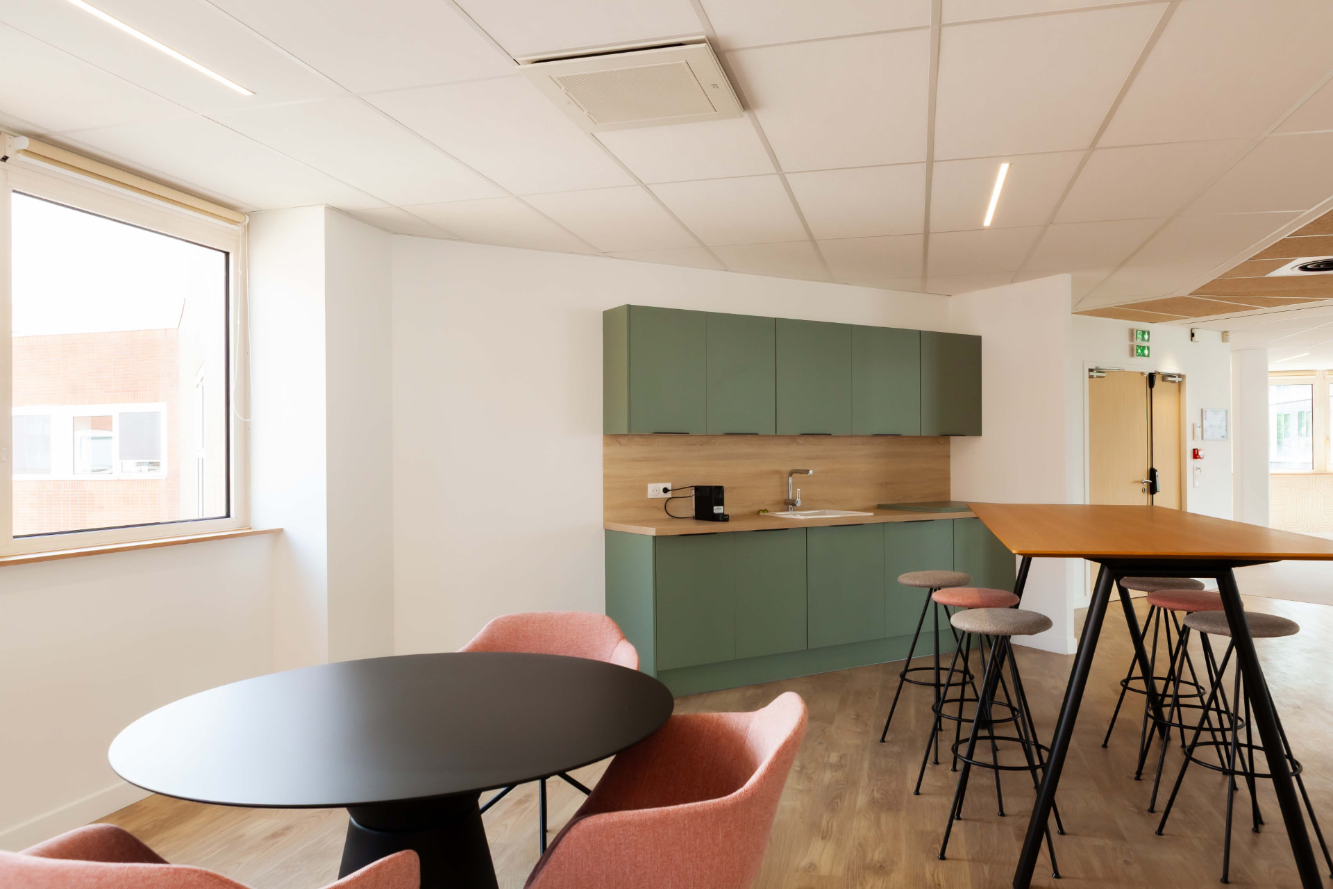 CLS Inside — breakroom with sage green cabinetry and pink armchairs around a circular table