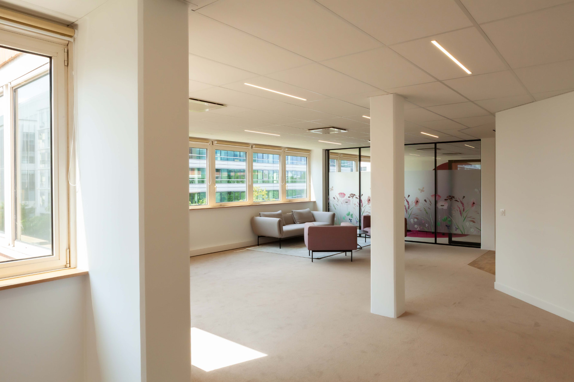 CLS Inside — office lounge with grey sofa and dusty rose armchairs under recessed lighting
